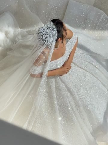 Bride in a sparkling white ball gown with intricate beading and a long veil, viewed from above as she gracefully holds her dress.” Why do brides wear white?