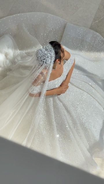 Bride in a sparkling white ball gown with intricate beading and a long veil, viewed from above as she gracefully holds her dress.” Why do brides wear white?
