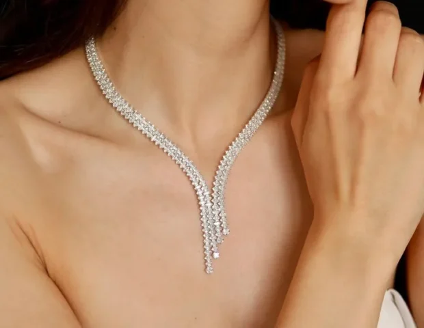 Budget Jewellery | Close-up of a bride wearing a silver-tone crystal zircon Y-shaped necklace with matching drop earrings and bracelet, in a strapless white dress, hand near chin.