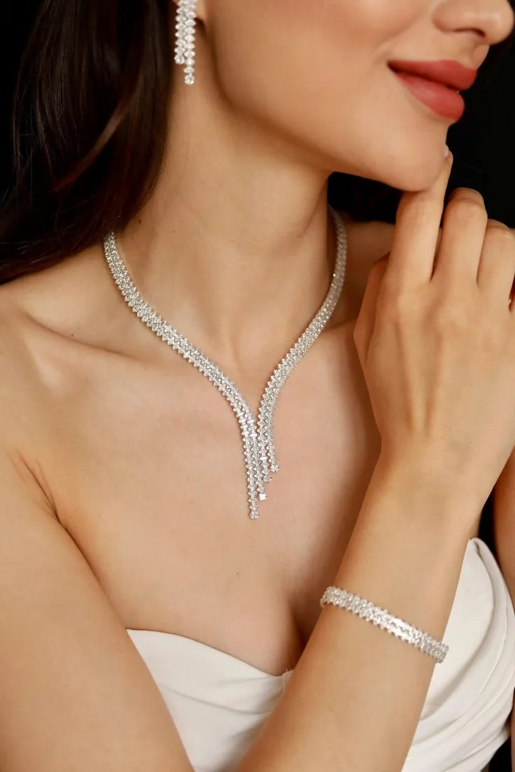 Budget Jewellery | Close-up of a bride wearing a silver-tone crystal zircon Y-shaped necklace with matching drop earrings and bracelet, in a strapless white dress, hand near chin.
