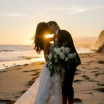 Beach Wedding | *Silhouette of a bride and groom standing under a floral arch on a beach at sunset, framed by tall palm trees, with guests seated on either side and the ocean glowing in the background.*