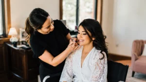 what every bride should know before booking a makeup artist | Sri Lankan bride-to-be receiving a natural bridal makeup trial from a professional makeup artist in a bright studio, surrounded by clean brushes, palettes, skincare products, false lashes, and bridal inspiration photos.