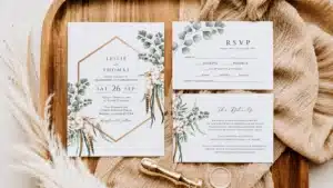 Wedding Invitation Etiquette | Elegant flat lay of wedding invitation stationery featuring an invitation card, RSVP card, details card, wax seal stamp, and botanical eucalyptus design arranged on a wooden tray with neutral fabric and pampas grass, creating a timeless and sophisticated wedding aesthetic.